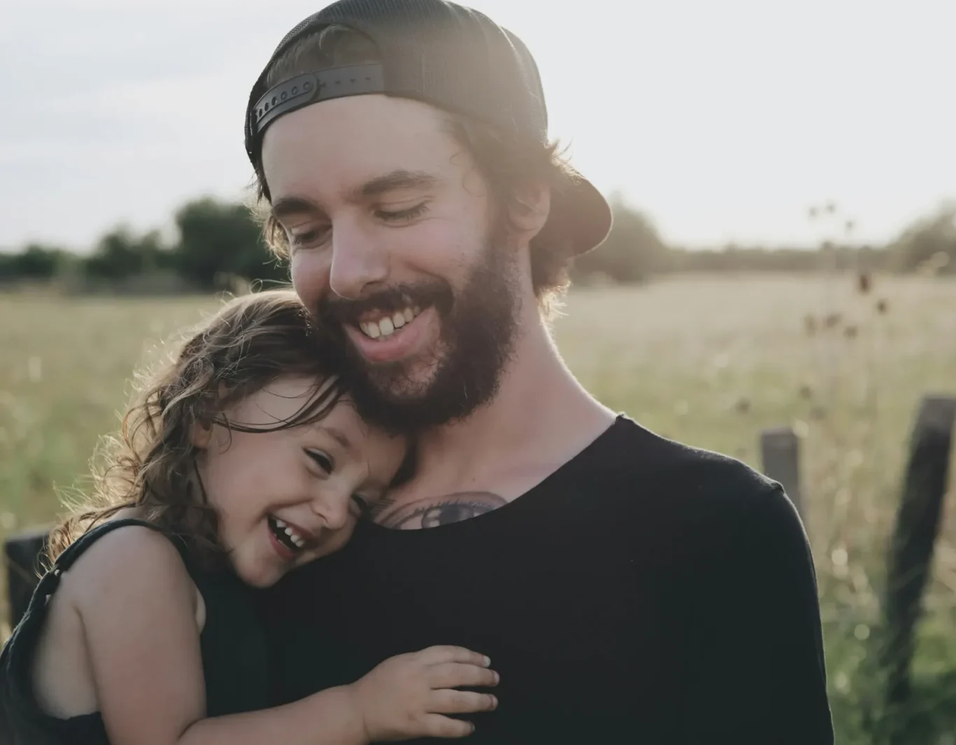 Die Mission der Value Heroes - Werthelden Junger Vater umarmt lächelnd sein Kind in einem Sonnenschein-Feld.