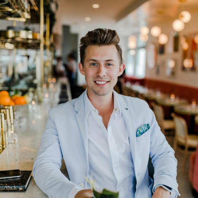 Kundenbewertung Lächelnder Mann in einem hellen Sakko, sitzt an einer Bar mit Getränk in der Hand.